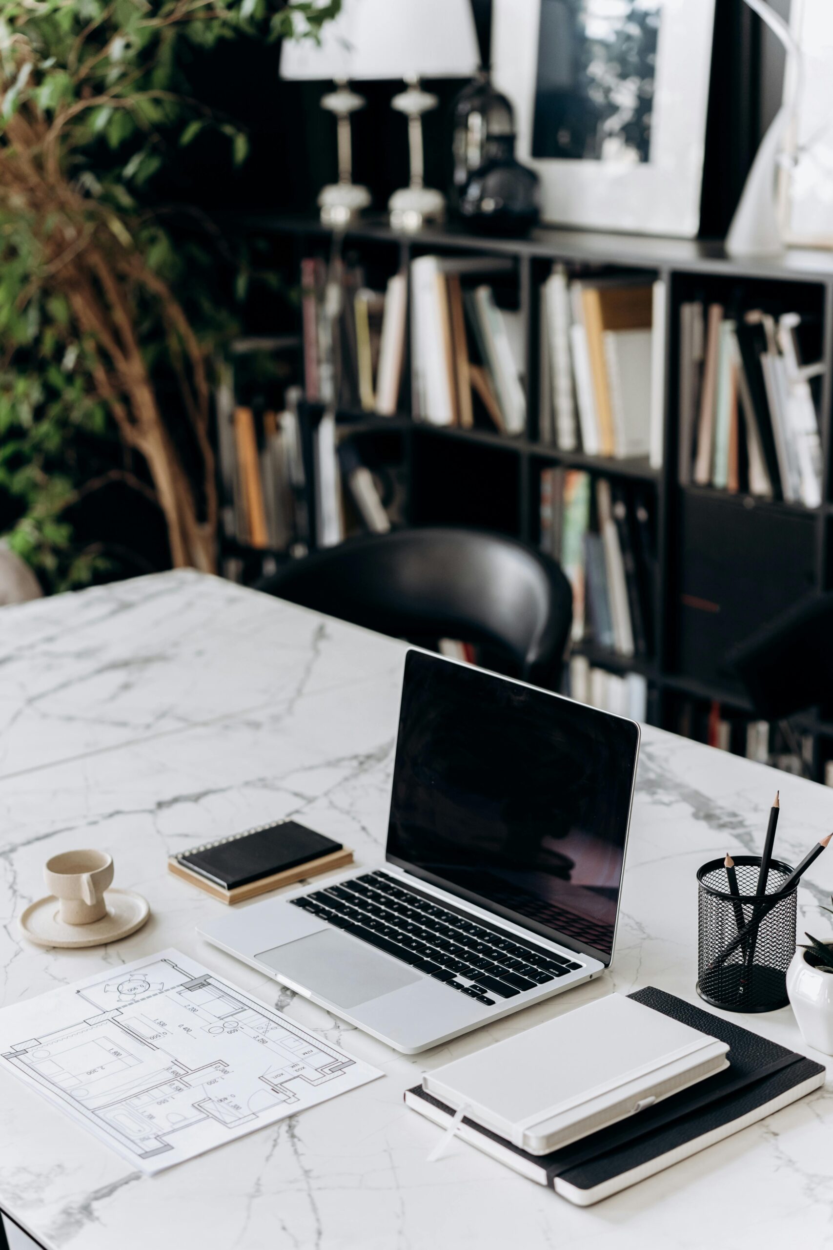 A modern minimalist workspace featuring a laptop, notebook, and coffee cup on a marble table.